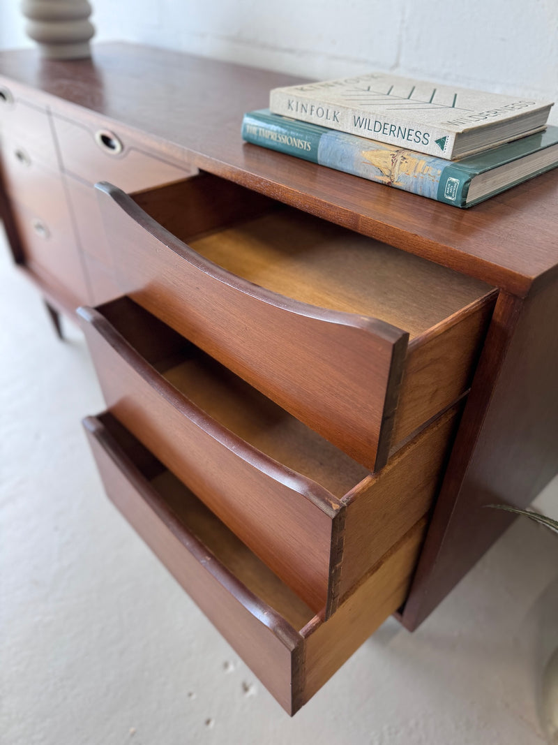Wooden dresser with open drawer and books on top against a white wall.